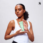 Woman holding a green skincare product against a plain background