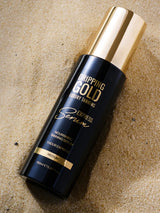Dripping Gold luxury tanning serum bottle on a sandy background