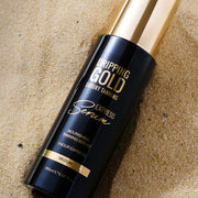 Dripping Gold luxury tanning serum bottle on a sandy background