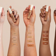 Five hands with different skin tones holding makeup products, showing color swatches on wrists.