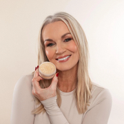Woman holding a jar of beige powder against a plain background