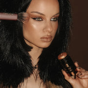 Woman applying makeup with a brush and compact mirror, wearing a fur-lined garment.