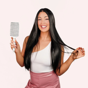 Woman with long black hair holding a hairbrush against a white background
